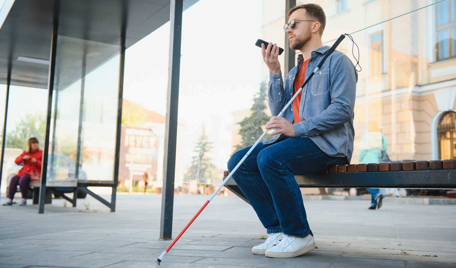 Una persona cieca su una panchina paerla al telefono